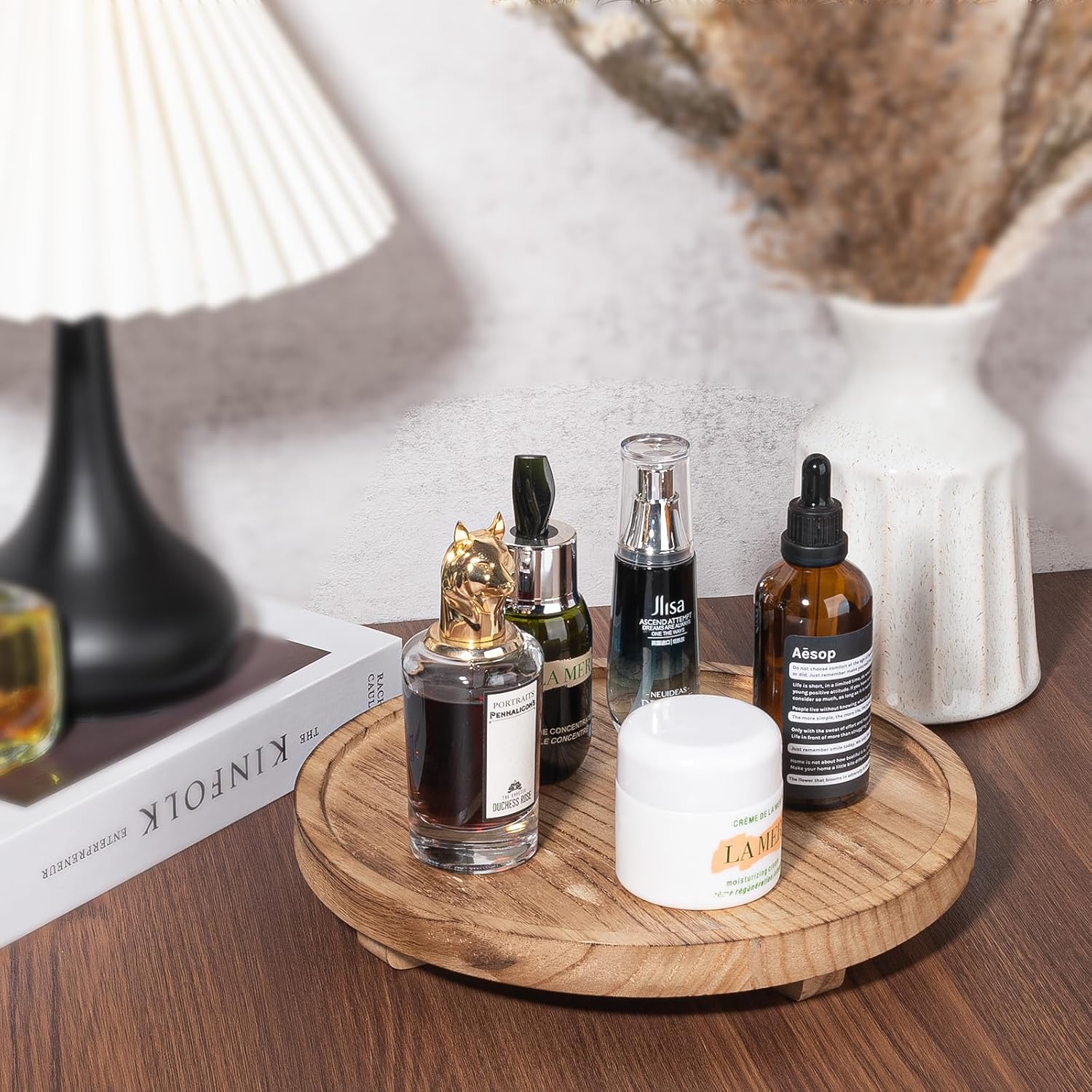 Collection of skincare and fragrance products on a wooden tray with a lamp and books in the background.