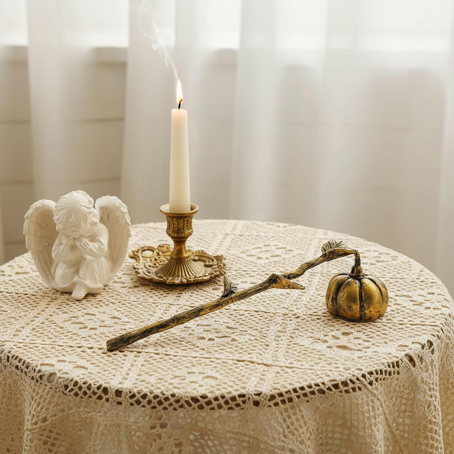 Decorative items on a table with a lace tablecloth, including a candle, angel figurine, and small pumpkin.