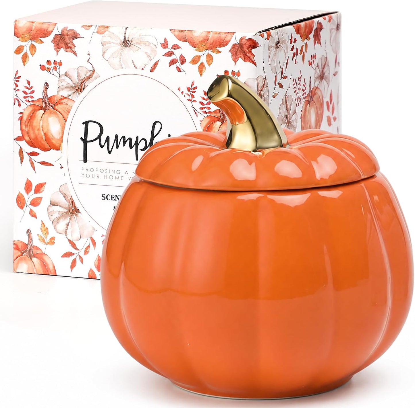 An orange pumpkin-shaped scented candle jar with a lid and a gold-toned stem, shown in front of its illustrated retail box on a white background.